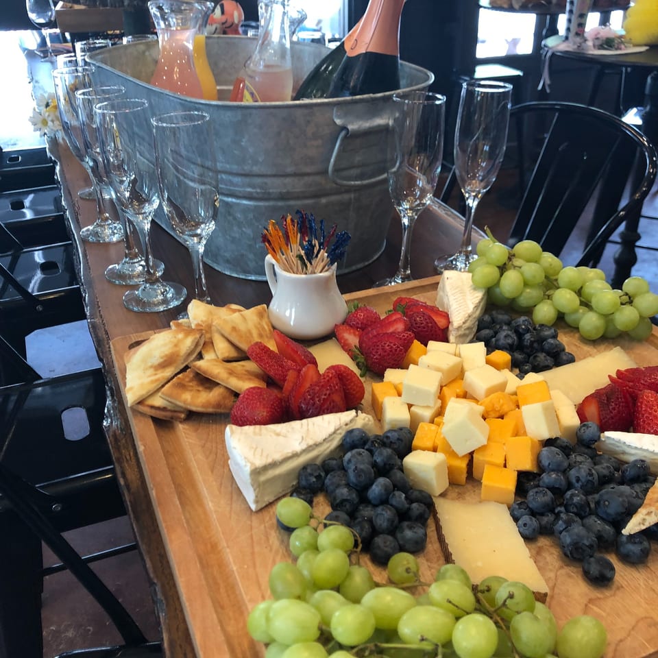 Restaurant buffet featuring a champagne bucket, flute glasses, assorted cheeses, crackers, grapes, strawberries, and blueberries.