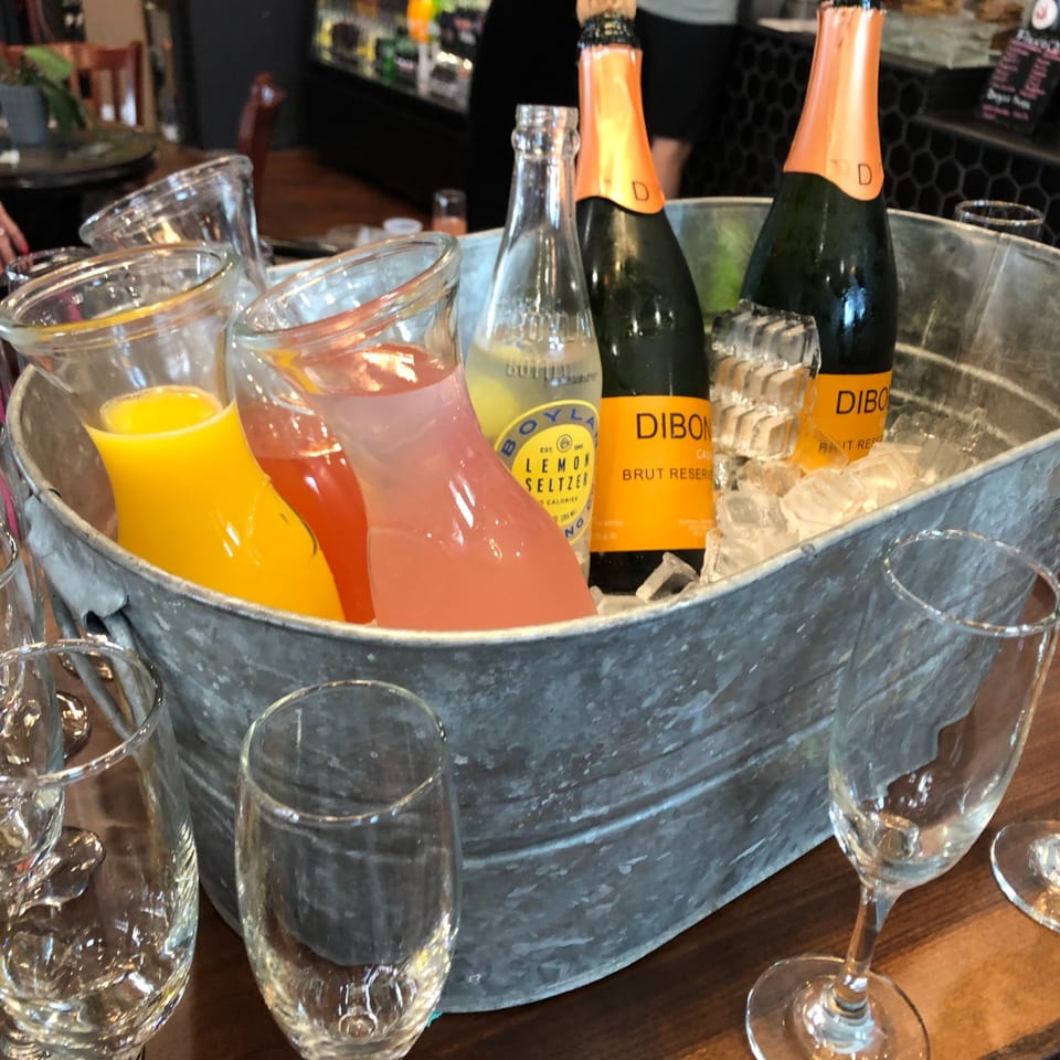 Sparkling wine and juice pitchers chilled in a tub with glasses.